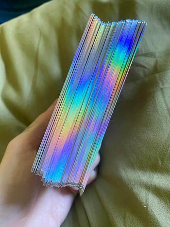 A manus  holds a stack of colorful holographic cards, shimmering successful  the light