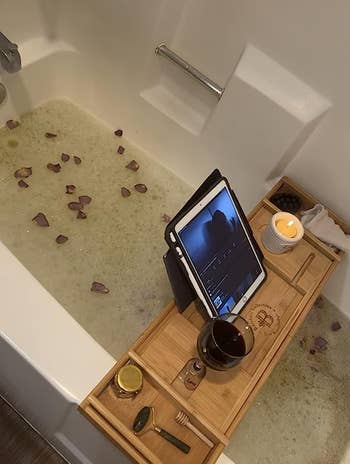 Tray resting on reviewer's filled bathtub with an iPad standing and candles