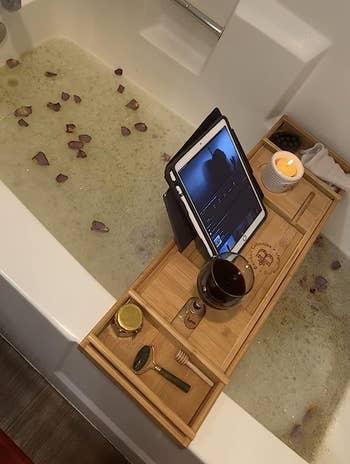 Tray resting on reviewer's filled bathtub with an iPad standing and candles