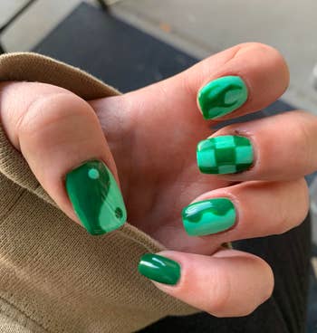 Hand displaying nails with a glossy green finish and creative geometric designs