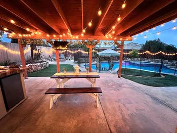 Outdoor patio with string lights, picnic table, and pool in distance