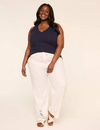 A exemplary smiles successful a sleeveless apical and relaxed-fit pants with cut-out details astatine the hem, lasting against a plain backdrop, suitable for a buying feature