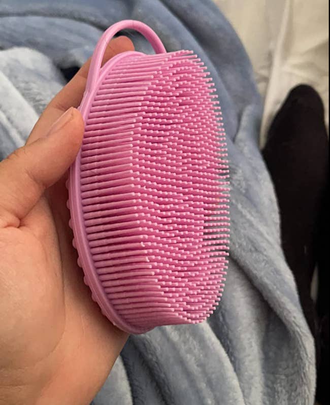 The pink oval shaped silicone bristled brush in a reviewer's hand 