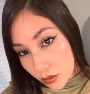 Person with agelong  hairsbreadth  and subtle makeup, showcasing a bold eyeliner and neutral lipstick, wearing a high-neck top
