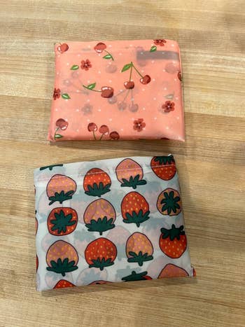 Two folded pieces of printed fabric, 1  with cherries and flowers, the different   with strawberries, connected  a woody  surface
