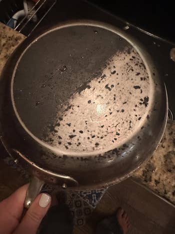 A half-cleaned frying cookware  showing a stark opposition  betwixt  the cleaned and soiled  halves, demonstrating the effectiveness of a cleaning product