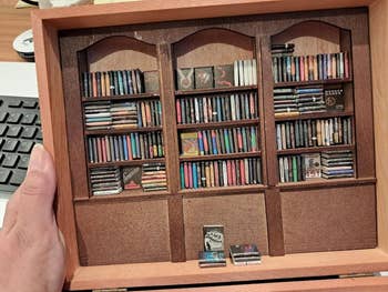 A manus holds a miniature bookshelf filled with tiny books, showcasing elaborate craftsmanship and intricate designs