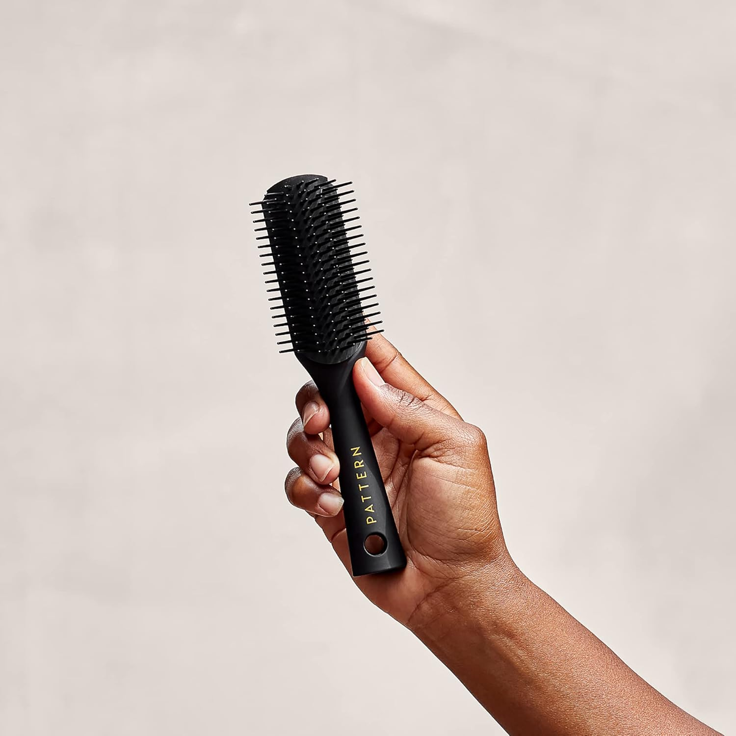 Hand holding a black styling brush with the brand name Pattern visible on the handle