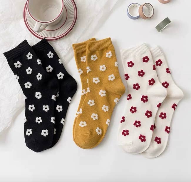 Three pairs of socks, one in black, one in yellow, and the other in white, all have small flowers on them