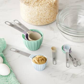 Measuring cups and spoons with rice, sugar, eggs, and solid bowls connected a room counter, suggesting baking essentials
