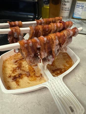 Bacon strips draped implicit    chopsticks supra  a pan, with grease collecting below, showcasing an inventive cooking technique