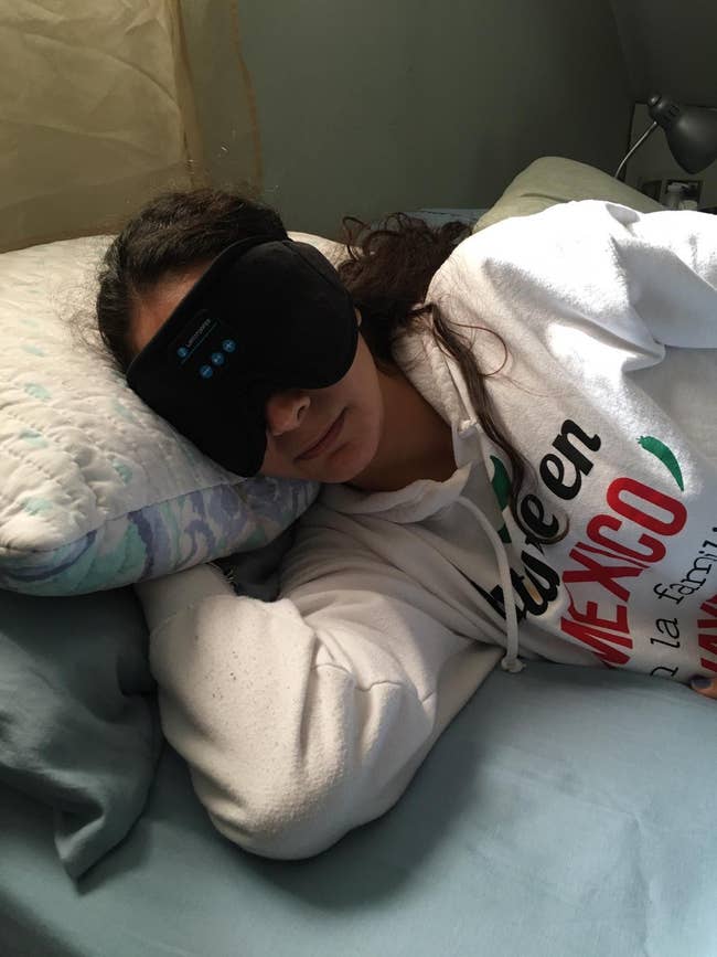 Person resting in bed with an eye mask on, wearing a sweatshirt