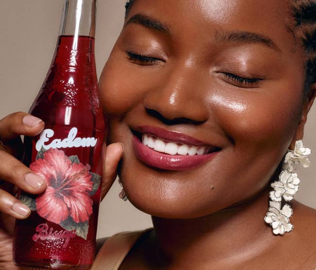 Person smiling while holding a bottle with a hibiscus design and