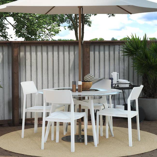 round outdoor able with an umbrella and white modern looking chairs