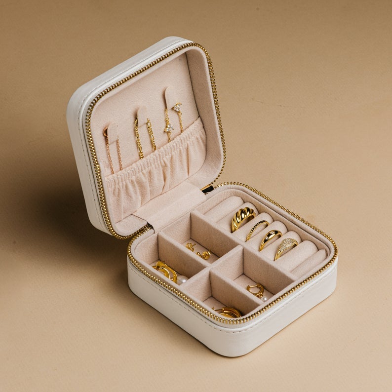small white jewelry box with a zip closure and some rings, earrings, and necklaces inside