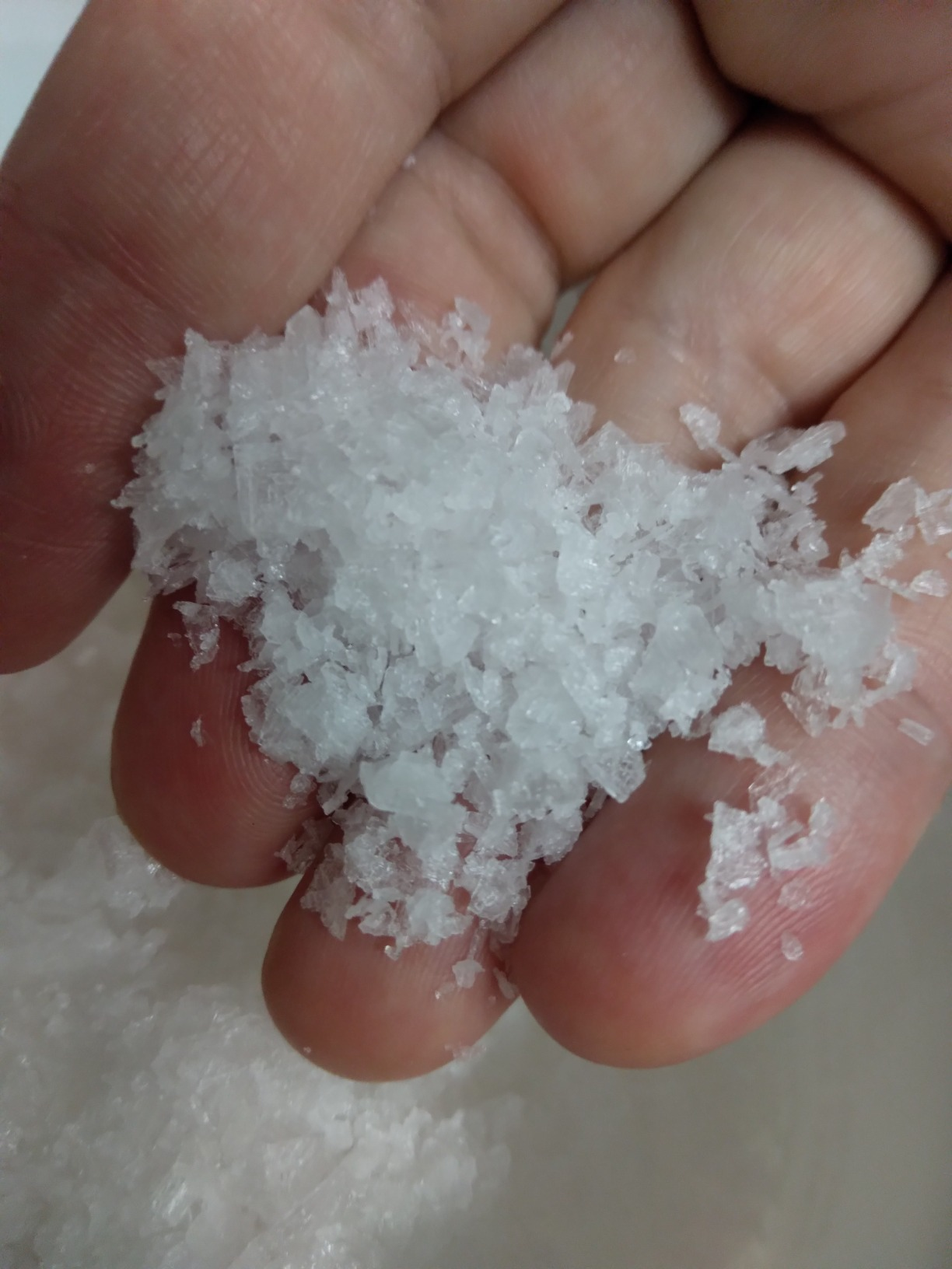 Close-up of a reviewer's hand holding Maldon sea salt, emphasizing it's large, flakey texture