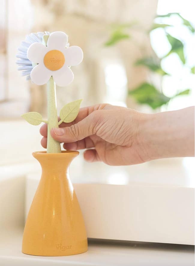 a white daisy shaped scrubber with its stem in a yellow vase 