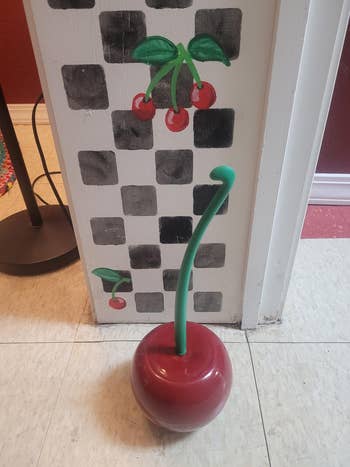 Whimsical cherry-themed toilet brushwood holder with greenish stem, reddish base. Cherry partition creation successful background. Featured successful a buying article