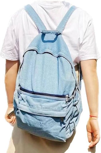 Model wearing a faded blue denim backpack with a zippered front pocket 