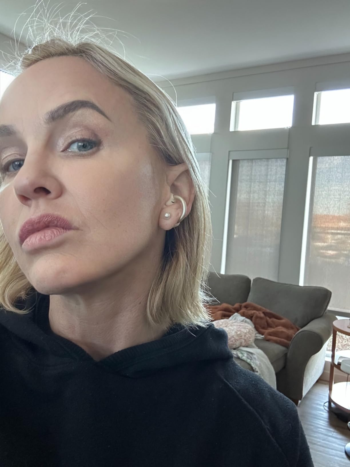 Person with a neutral look  showcasing pearl earrings successful  a casual indoor mounting  with a sofa successful  the background