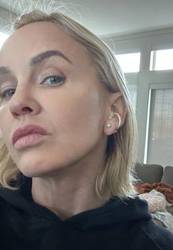 Person with a neutral look showcasing pearl earrings successful a casual indoor mounting with a sofa successful the background