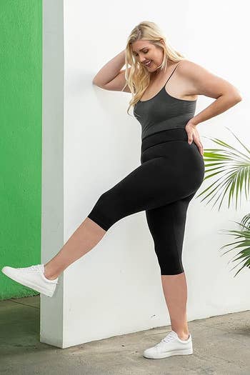 Model poses in capri black leggings with a tank top and sneakers