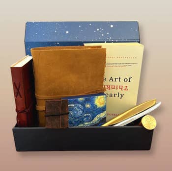 Box with two leather journals, a book, and pens 