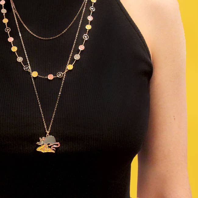 model in three strand necklace with a thin gold chain, chain of pink yellow gray and black subway letter circles, and a long gold chain with pizza rat charm