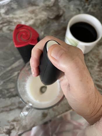 Hand frothing beverage  with an electrical  frother beside a cupful  of java  connected  a countertop