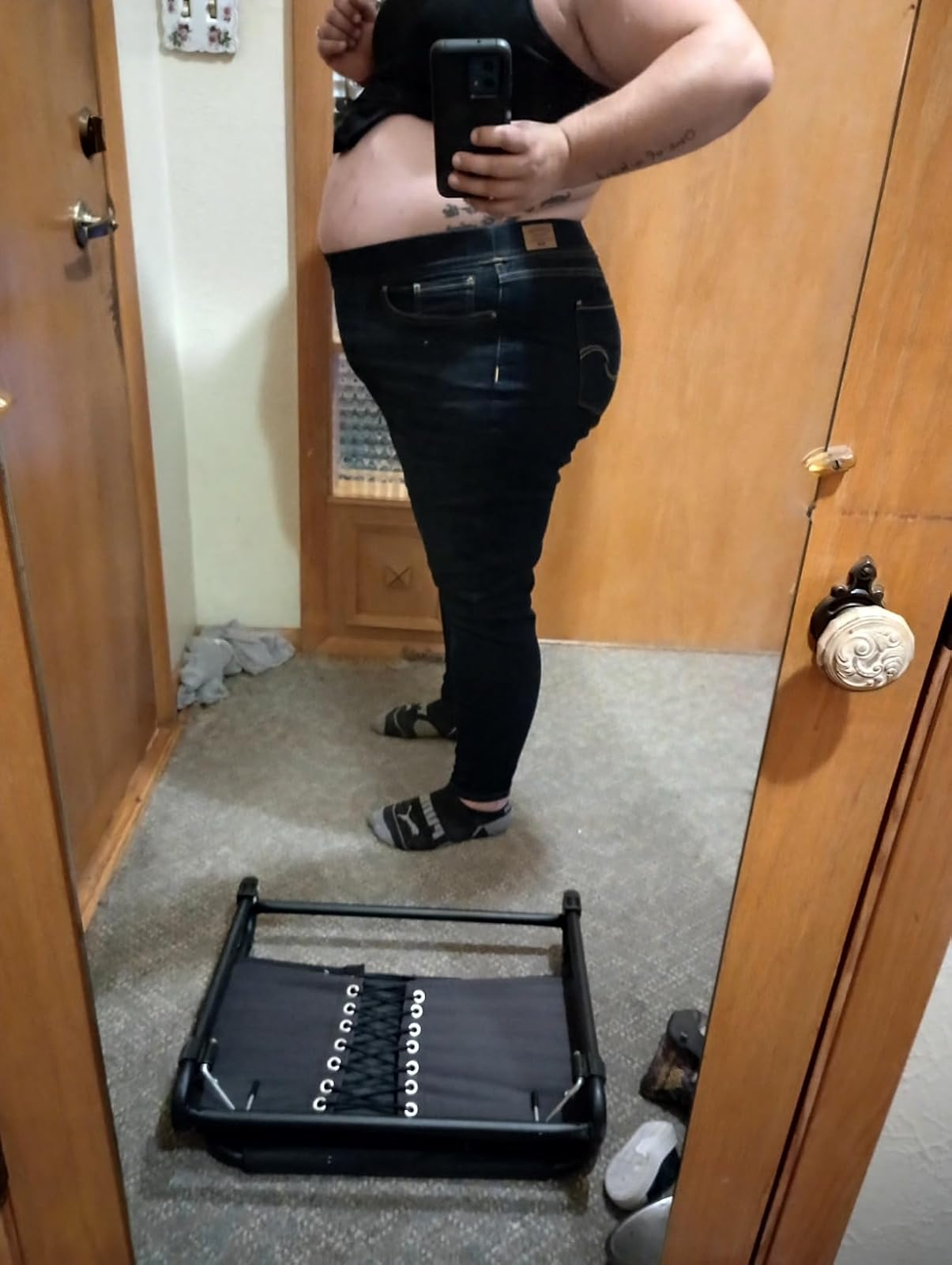 Person taking a reflector  selfie successful  a bedroom, wearing fitted jeans and a achromatic  top, lasting  adjacent   a tiny  workout  stepper