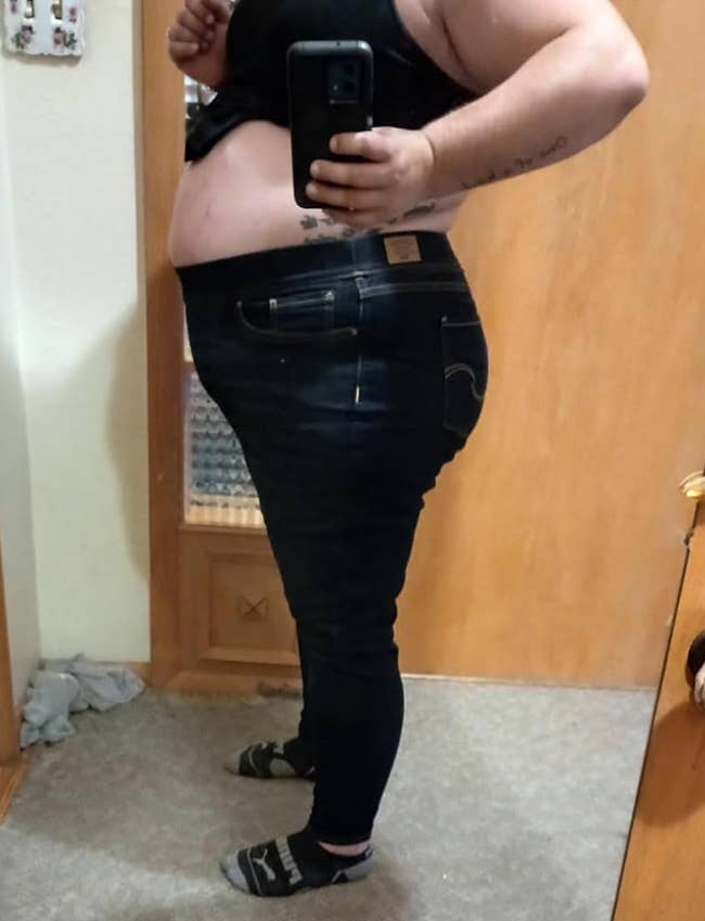 Person taking a reflector selfie successful a bedroom, wearing fitted jeans and a achromatic top, lasting adjacent a tiny workout stepper