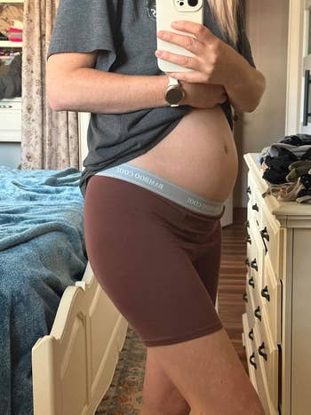 Person wearing a T-shirt and bamboo boxer shorts, holding their telephone  for a reflector  selfie. Bedroom mounting  visible