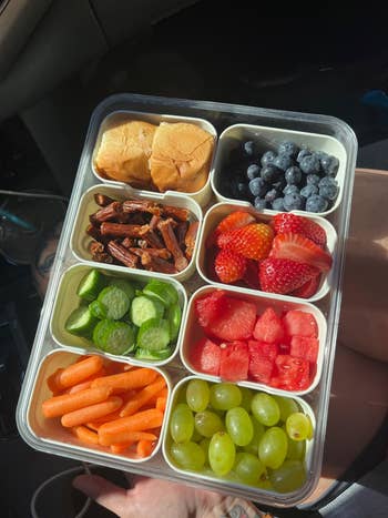 A bento-style snack tray with sliders, blueberries, strawberries, watermelon, grapes, mini cucumbers, carrots, and jerky