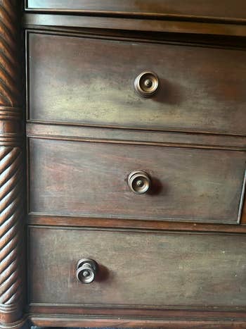 Close-up of a worn wooden dresser with three drawers and round knobs