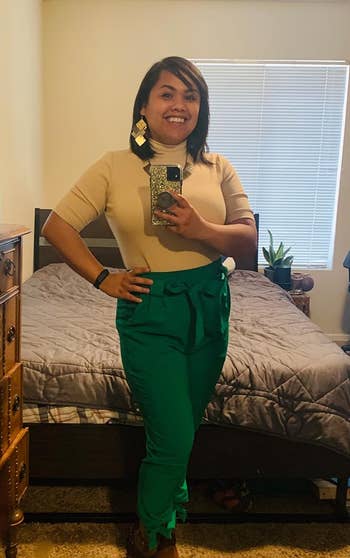 Reviewer wearing a beige top, green high-waisted pants, and brown boots