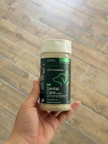 Person holding a container of VetriScience Dental Care Powder for pets, highlighting its dental health benefits for cats and dogs