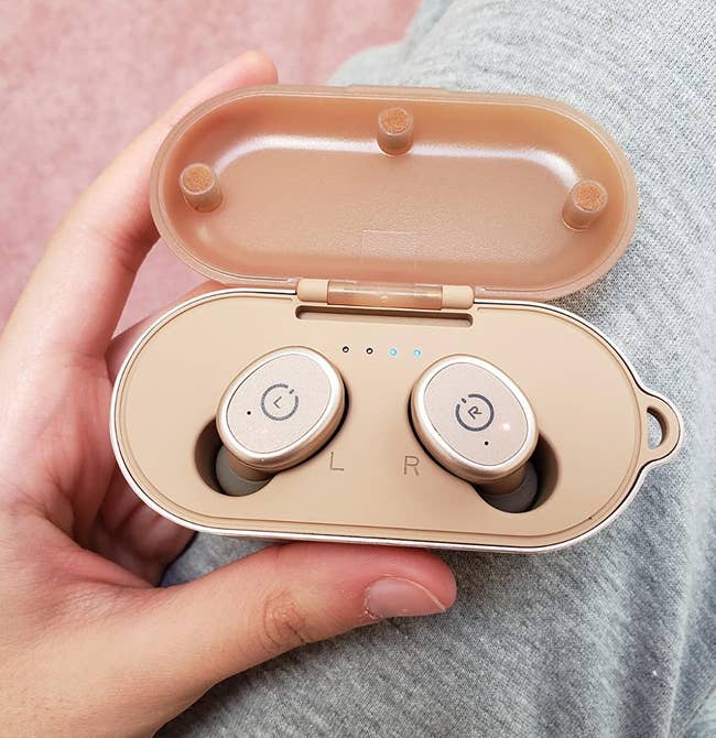 reviewer holding the rose gold earbuds in their charging case