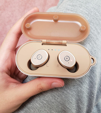 reviewer holding the rose gold earbuds in their charging case