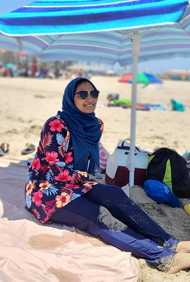 Reviewer is wearing the burkini in a navy blue color with red and yellow tropical flowers on the top