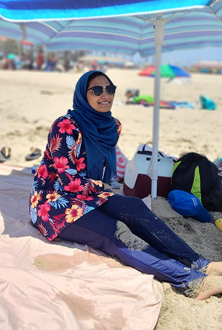 Reviewer is wearing the burkini in a navy blue color with red and yellow tropical flowers on the top
