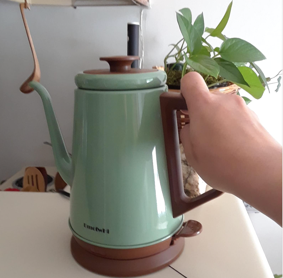 Reviewer holding lid of pale seafoam green kettle  with brown accents 