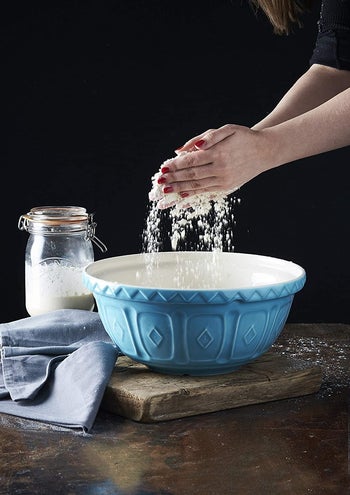 hands sifting flour over the blue mixing bowl