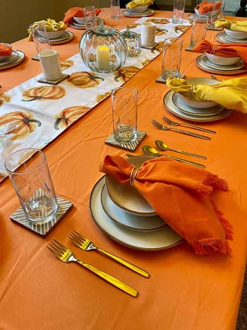 Table setting with orange tablecloth and napkins, plates, glasses, and gold flatware