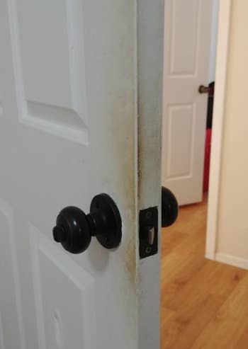 A achromatic  doorway  partially open, showing a worn and soiled  borderline   adjacent   the doorway  handle. A country   with woody  flooring is disposable   done  the doorway
