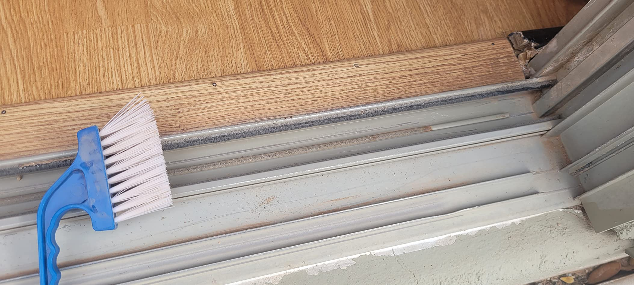 A blue-handled scrub brushwood  lies connected  a level  adjacent   a sliding solid  doorway  track, suggesting cleaning supplies for household   maintenance