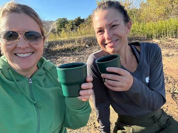Two people smiling, holding green camping mugs outdoors