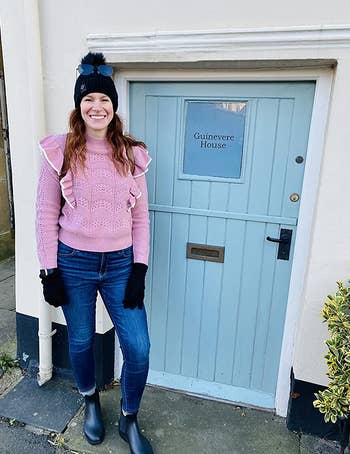 reviewer wearing the black boots with jeans and a pink sweater next to a blue door