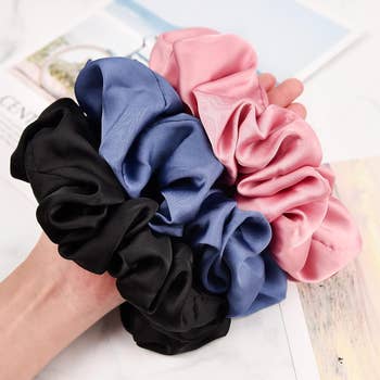 models hand holding the black, blue, and pink scrunchies