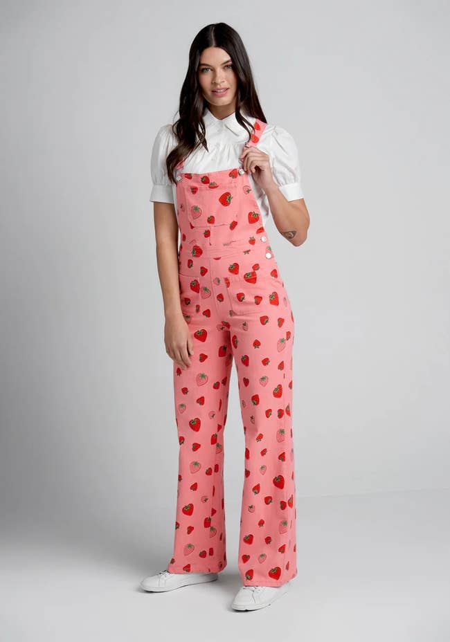model in pink and red strawberry print overalls with pockets