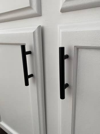 Close-up of sleek black cabinet handles on a textured white cabinet surface